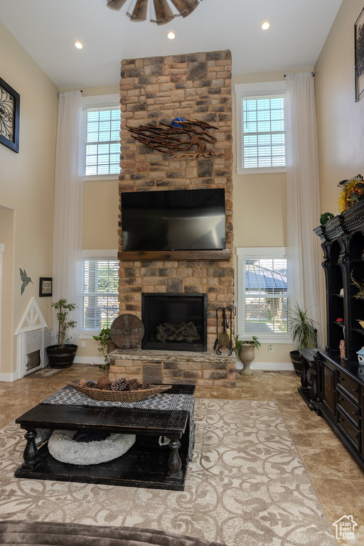 Living room featuring a high ceiling, a stone fireplace, plenty of natural light, and recessed lighting