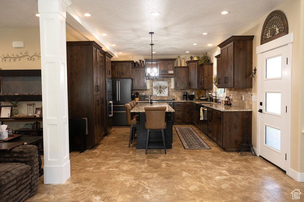 Kitchen featuring high end refrigerator, plenty of natural light, dark brown cabinets, a center island with sink, and recessed lighting