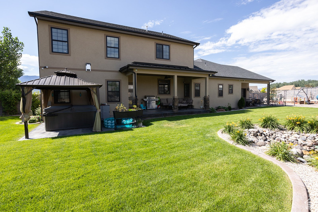 Rear view of property with a patio area, a gazebo, stucco siding, and a yard