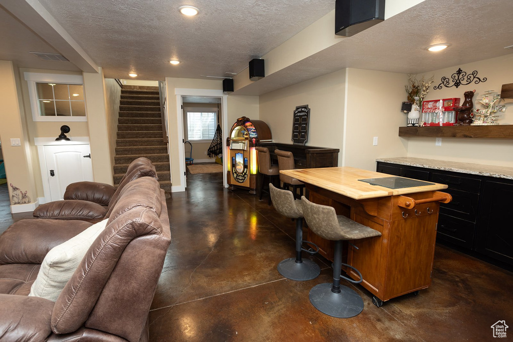 Indoor bar with finished concrete flooring, a textured ceiling, stairway, and recessed lighting