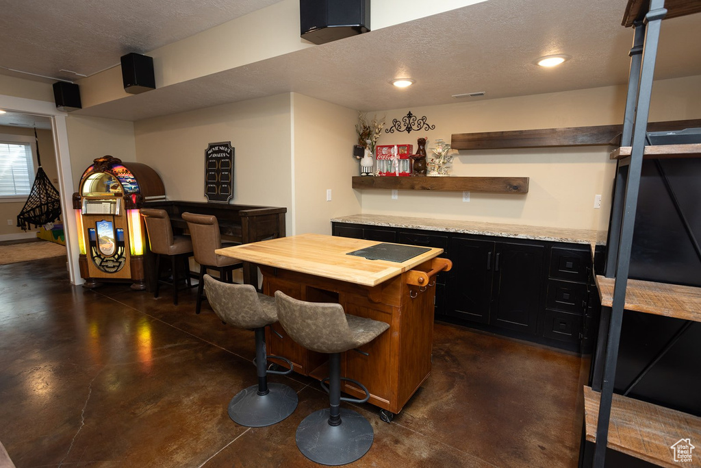 Indoor bar with concrete flooring, a textured ceiling, and recessed lighting
