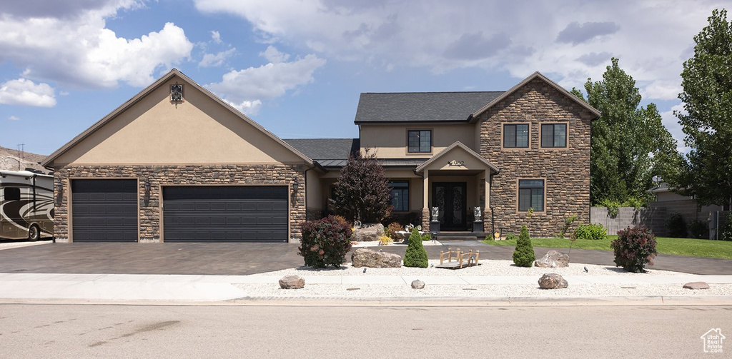 View of front of property featuring stucco siding, stone siding, a garage, and driveway
