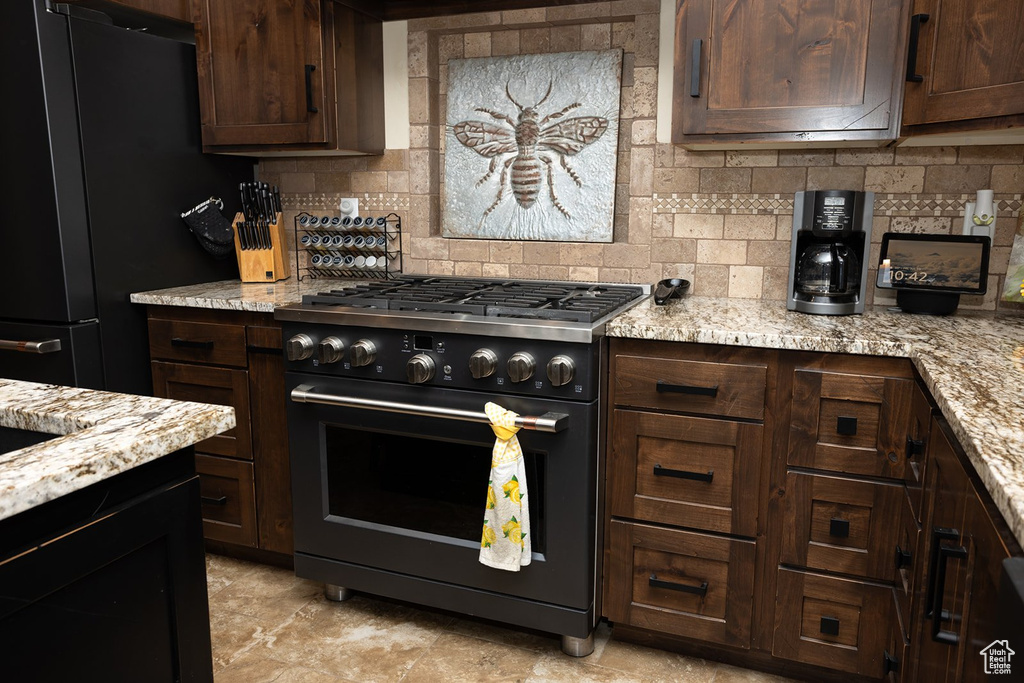 Kitchen with range with gas stovetop, freestanding refrigerator, backsplash, dark brown cabinetry, and light stone counters