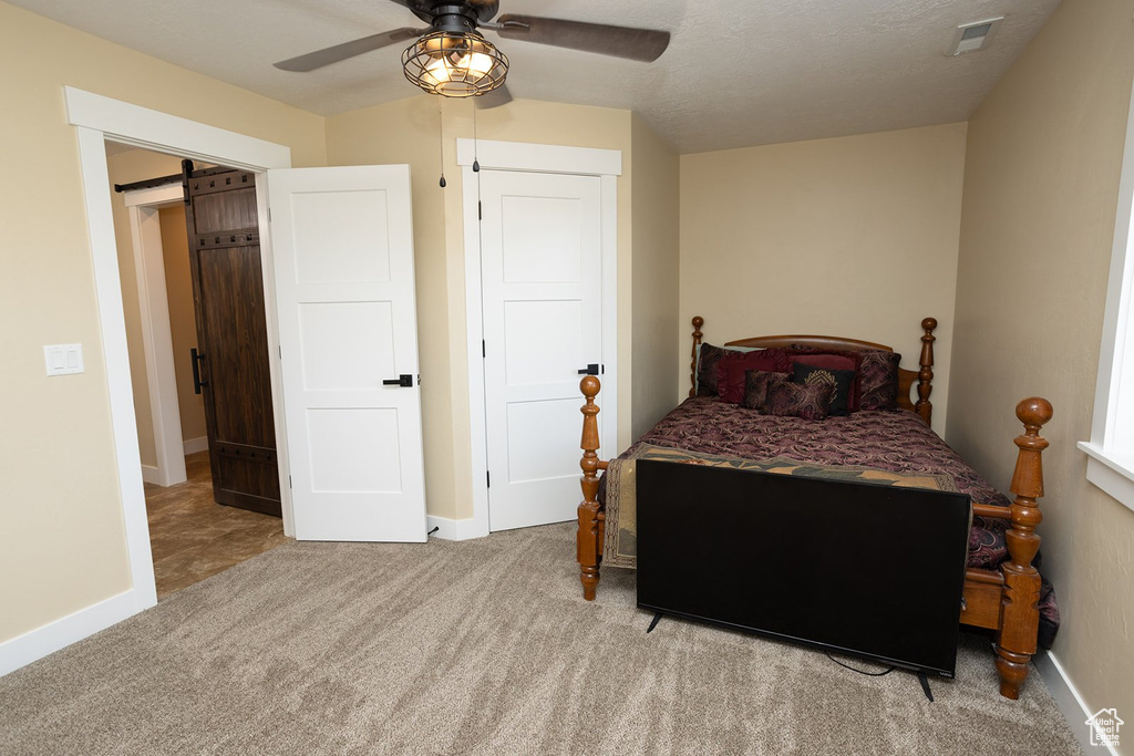 Carpeted bedroom featuring a barn door and ceiling fan