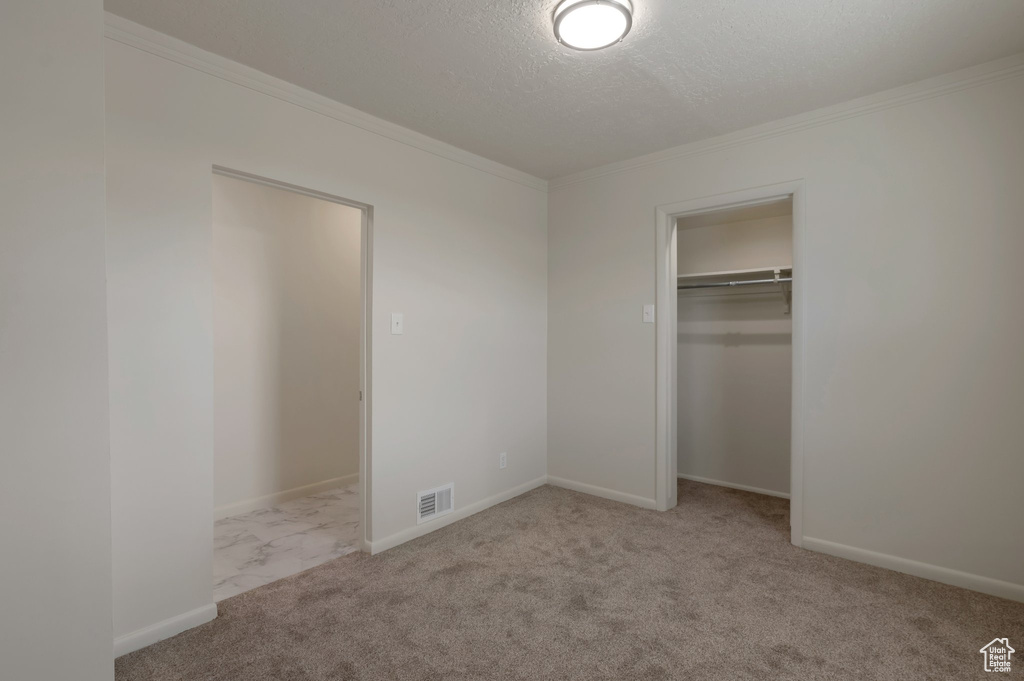 Unfurnished bedroom with ornamental molding, a textured ceiling, carpet flooring, and a closet