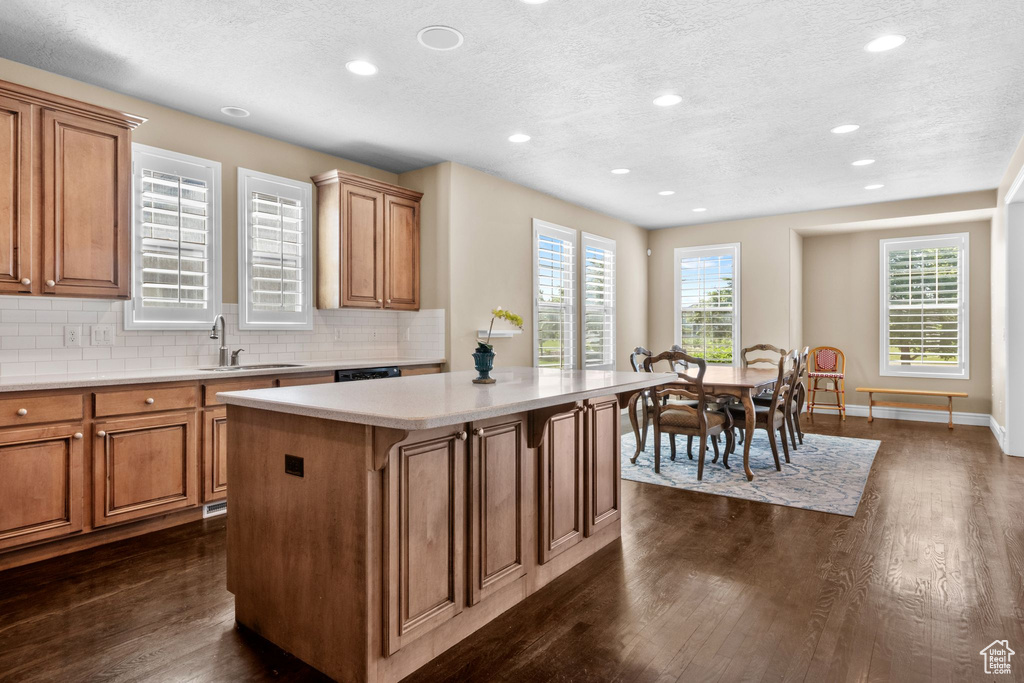 Kitchen with a textured ceiling, dark wood-style flooring, recessed lighting, a center island, and brown cabinetry