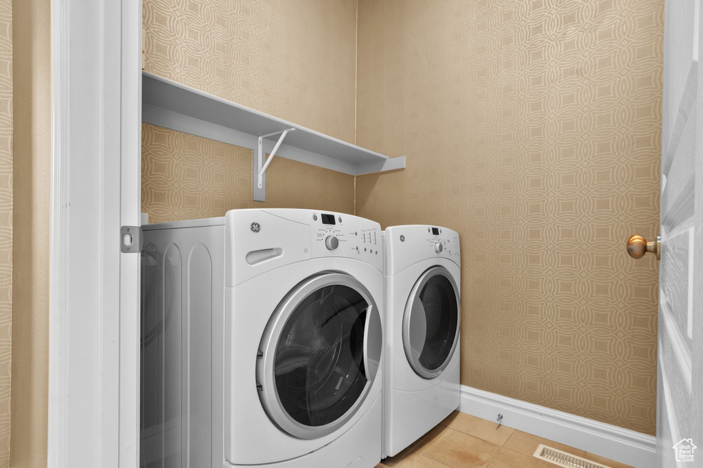 Washroom with washing machine and clothes dryer, wallpapered walls, and light tile patterned floors