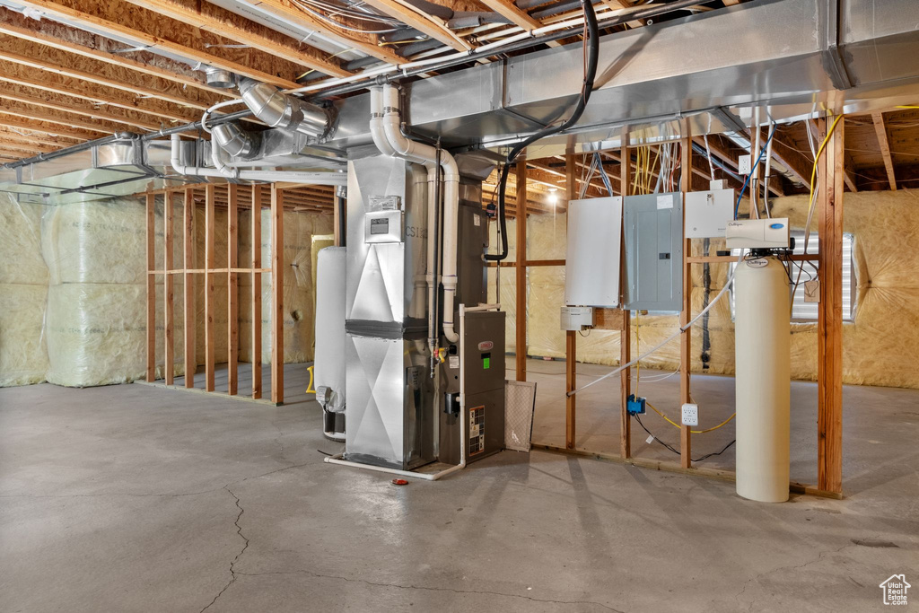 Unfinished basement featuring electric panel, heating unit, a water softener system, and water heater