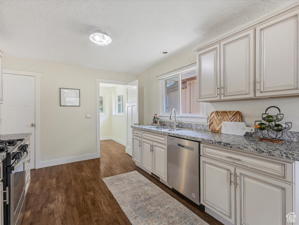 Kitchen featuring stainless steel appliances, dark wood-style flooring, cream cabinetry, and light stone counters