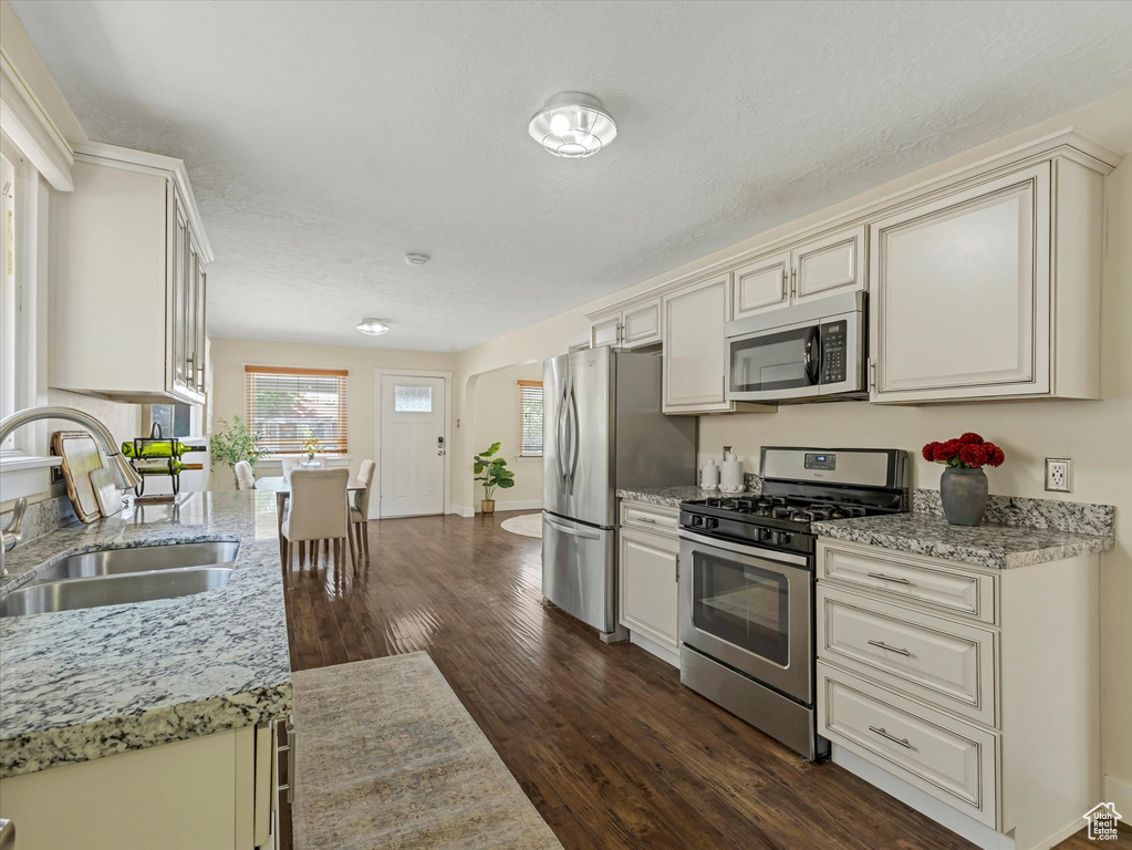 Kitchen with appliances with stainless steel finishes, dark wood finished floors, light stone counters, and cream cabinets