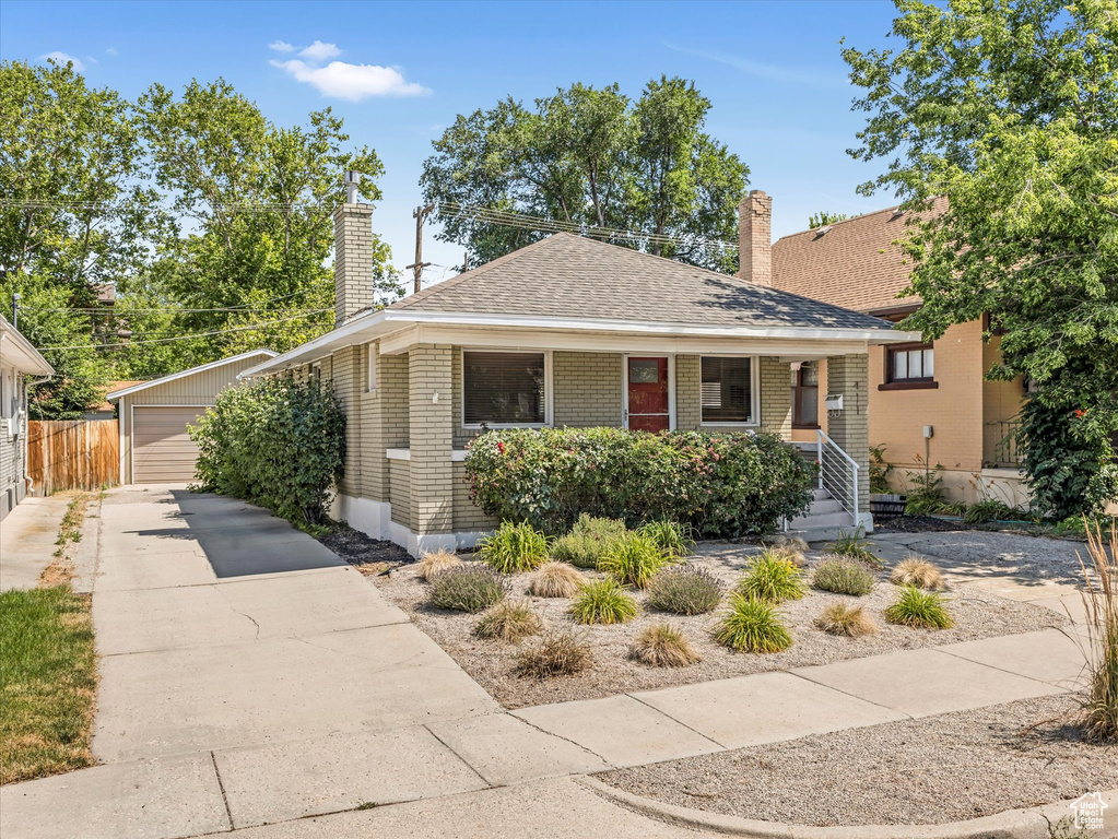 View of front of property featuring a chimney, brick siding, an outbuilding, a detached garage, and a shingled roof