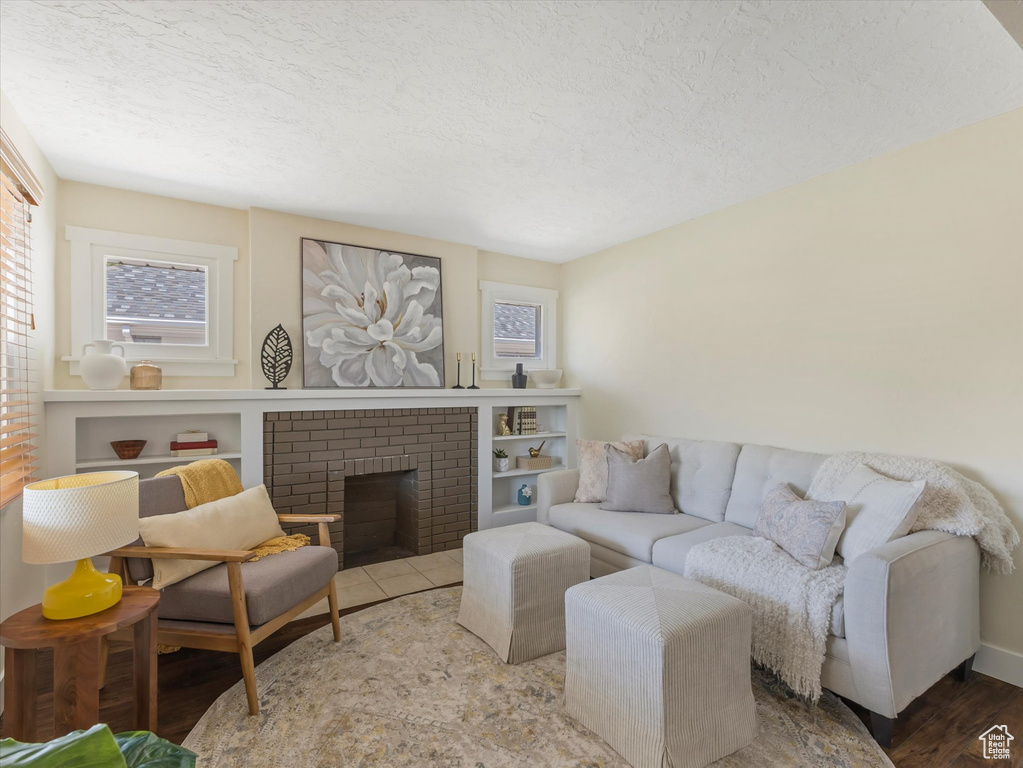 Living room featuring a textured ceiling, wood finished floors, and a brick fireplace