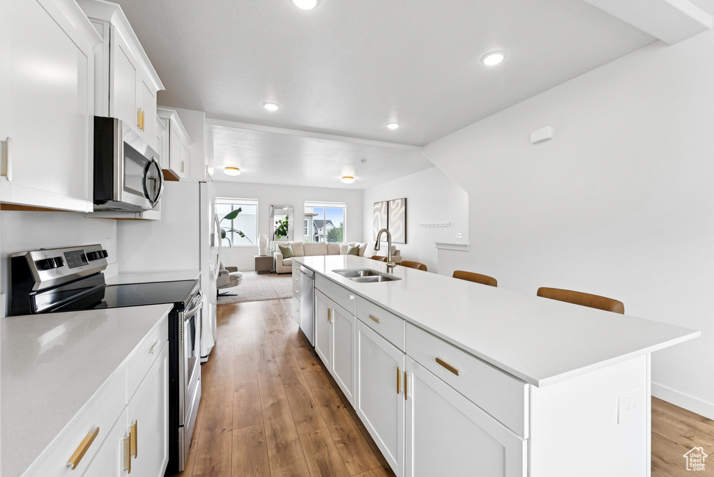 Kitchen featuring stainless steel appliances, open floor plan, recessed lighting, white cabinets, and light wood-type flooring