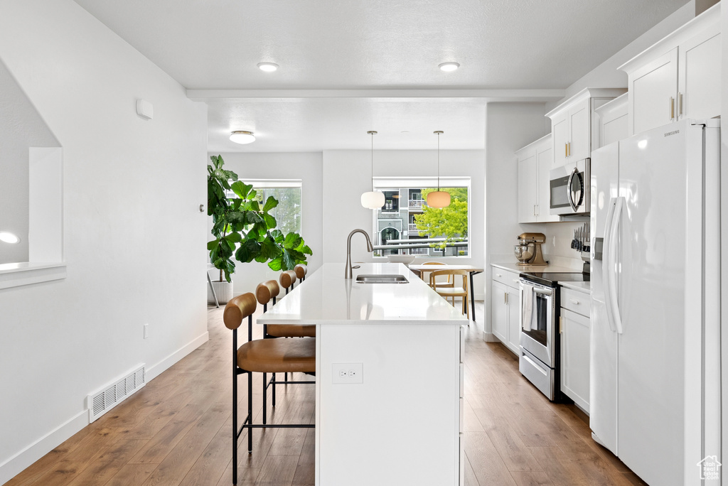 Kitchen with appliances with stainless steel finishes, a breakfast bar area, a center island with sink, wood finished floors, and white cabinetry