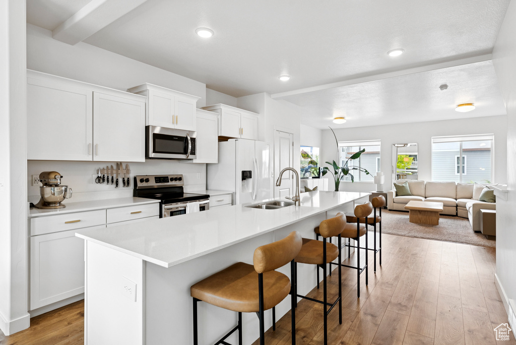Kitchen featuring stainless steel appliances, a breakfast bar area, a center island with sink, light countertops, and white cabinets