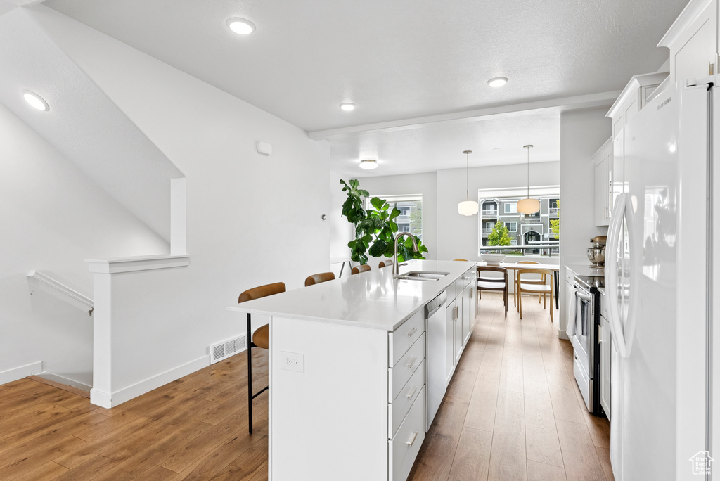 Kitchen featuring freestanding refrigerator, a breakfast bar area, light wood finished floors, white cabinets, and an island with sink