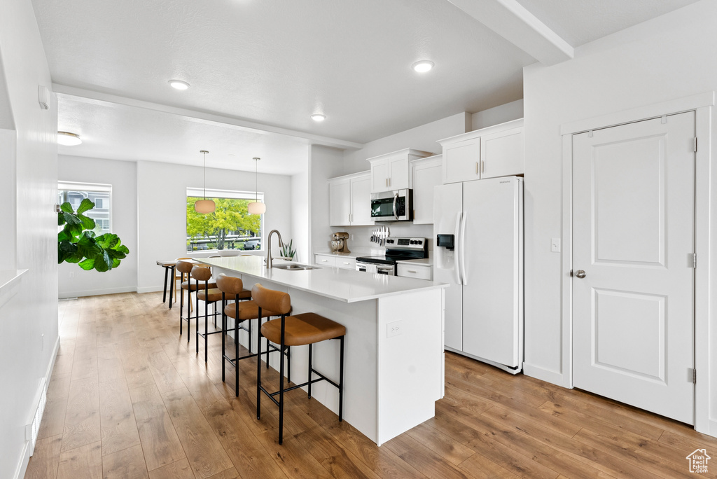 Kitchen featuring appliances with stainless steel finishes, an island with sink, a breakfast bar area, white cabinetry, and light wood-style floors