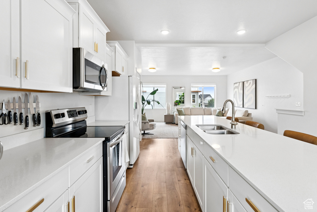 Kitchen featuring stainless steel appliances, open floor plan, white cabinets, light wood-style flooring, and light countertops