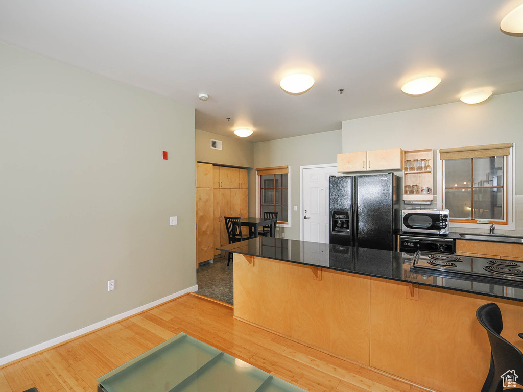 Kitchen featuring black fridge, stainless steel microwave, a sink, a kitchen bar, and light wood finished floors