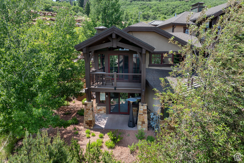 View of front of home with stucco siding, a patio area, a view of trees, and roof with shingles