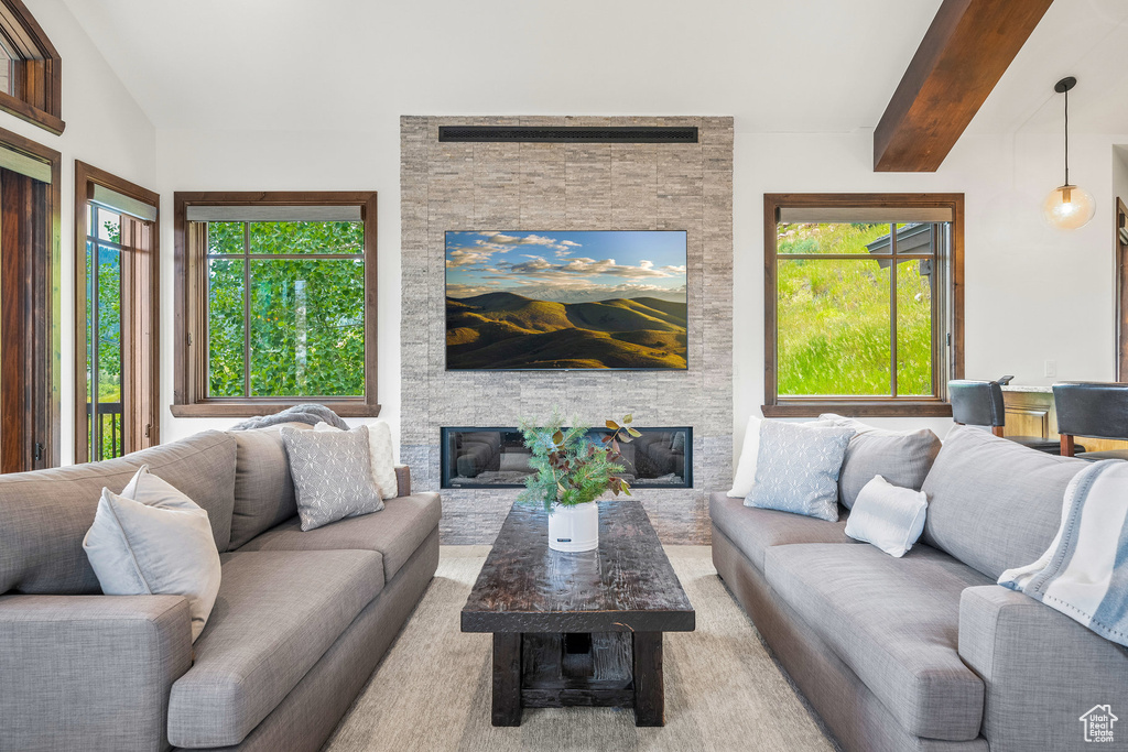 Living area with a stone fireplace, plenty of natural light, and beam ceiling