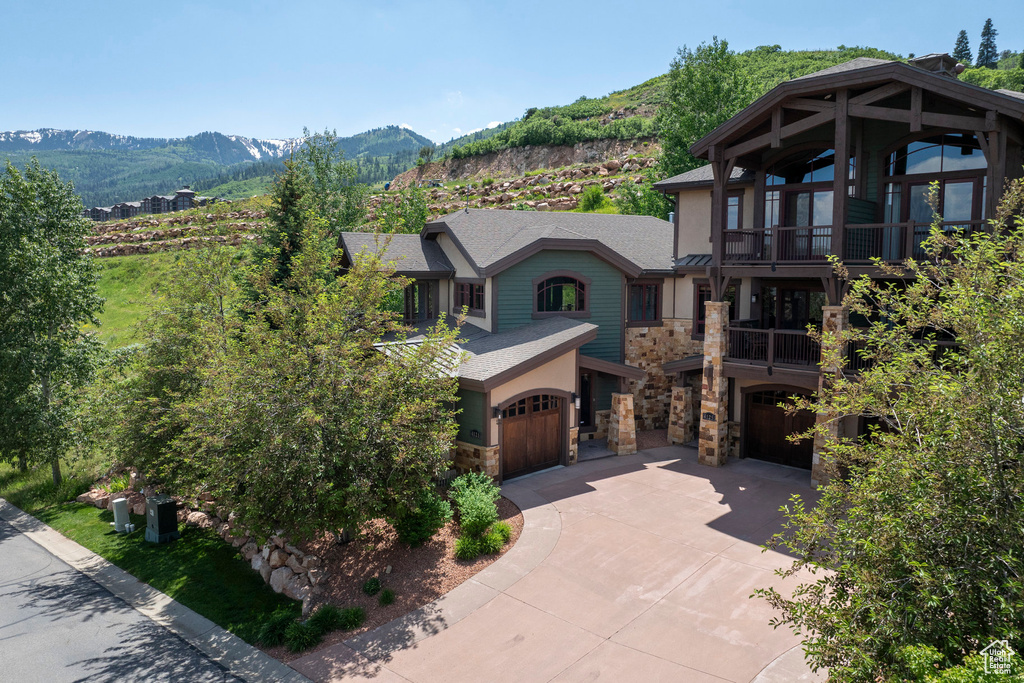 View of front of property featuring stone siding, a balcony, a garage, concrete driveway, and a mountain view