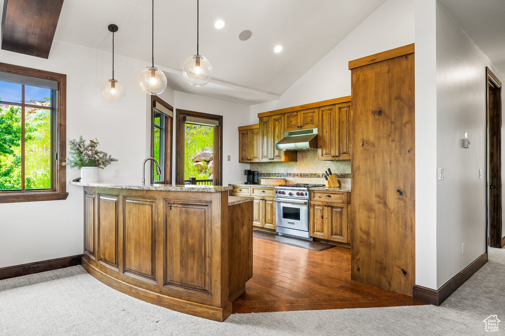 Kitchen with stainless steel range, under cabinet range hood, brown cabinets, a peninsula, and vaulted ceiling