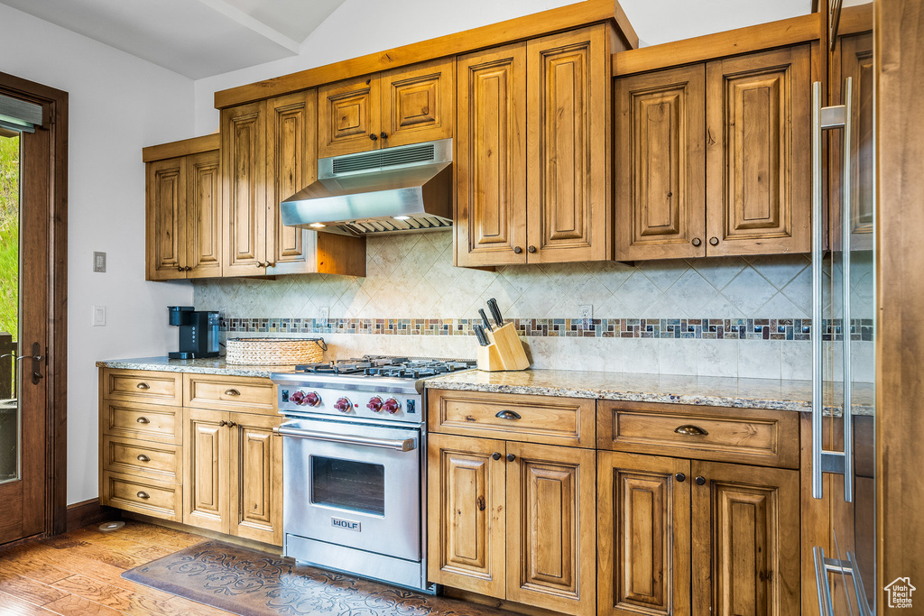Kitchen with premium range, under cabinet range hood, light wood-style floors, brown cabinetry, and lofted ceiling