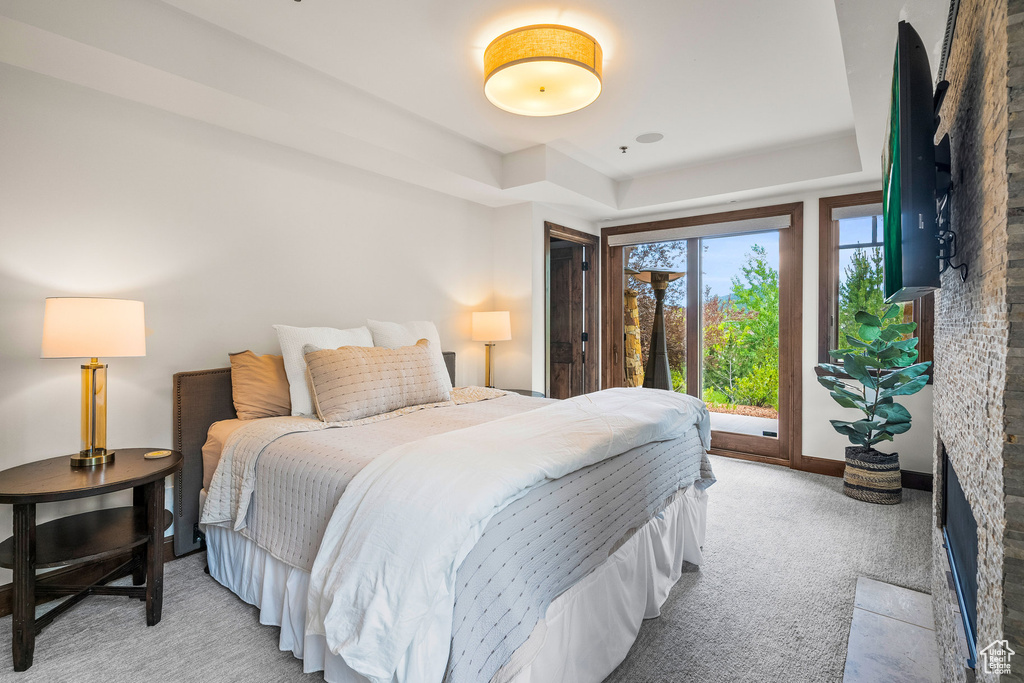 Bedroom with a raised ceiling, light carpet, access to exterior, and a fireplace