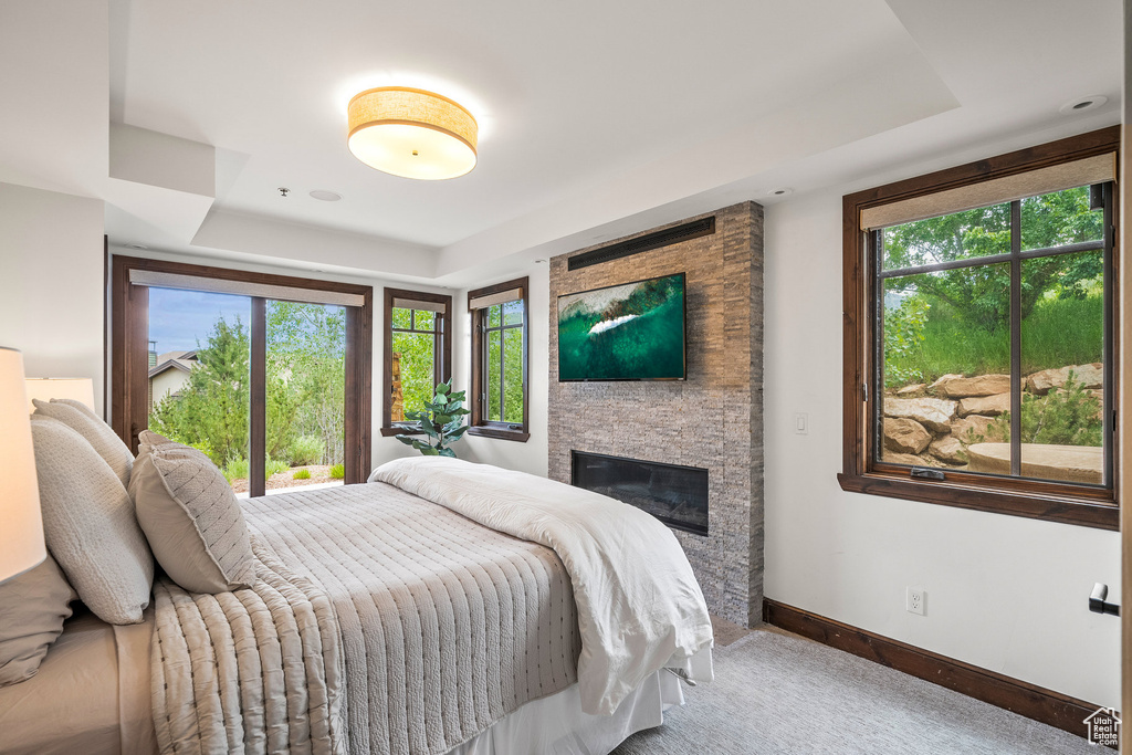 Bedroom with a raised ceiling, multiple windows, a fireplace, and carpet floors