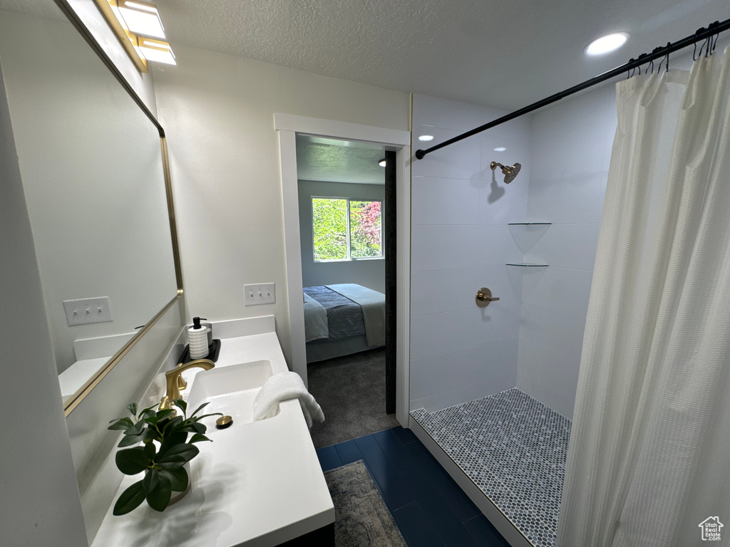 Ensuite bathroom featuring vanity, tiled shower, recessed lighting, wood finished floors, and a textured ceiling