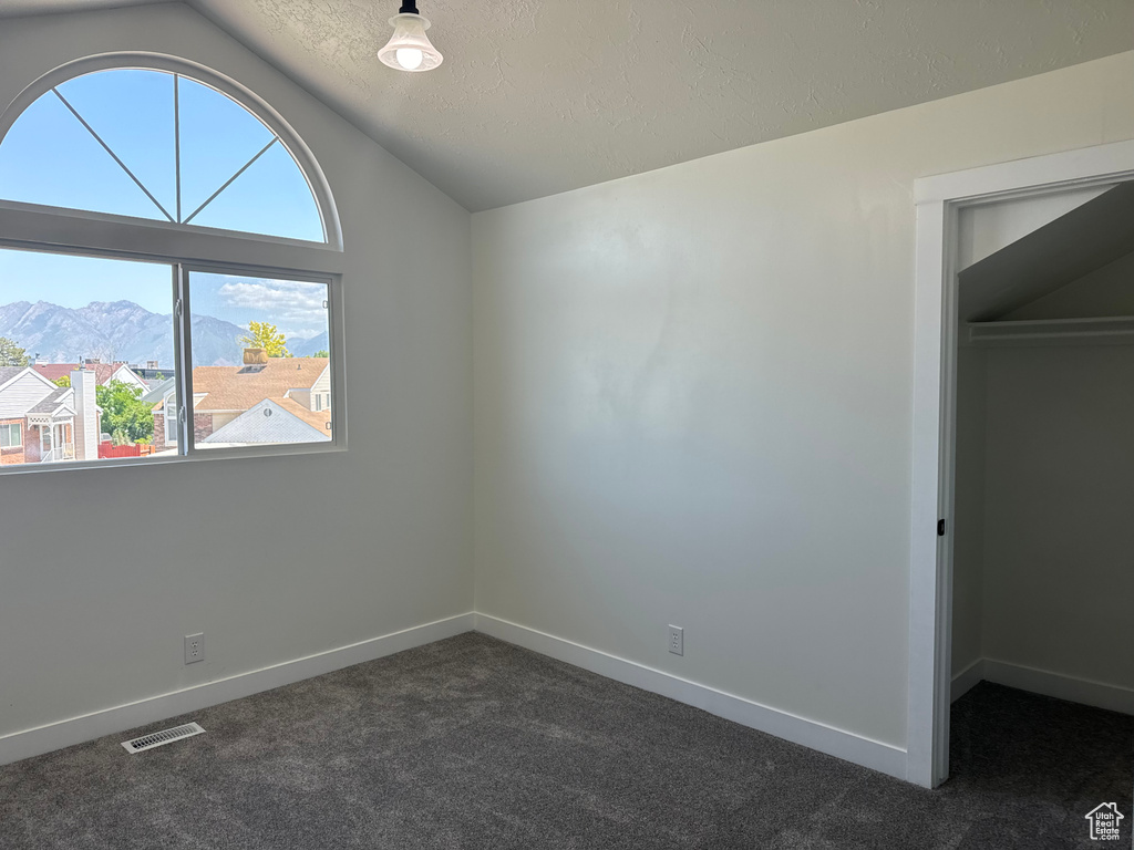 Unfurnished bedroom with vaulted ceiling, dark colored carpet, a textured ceiling, a walk in closet, and a mountain view