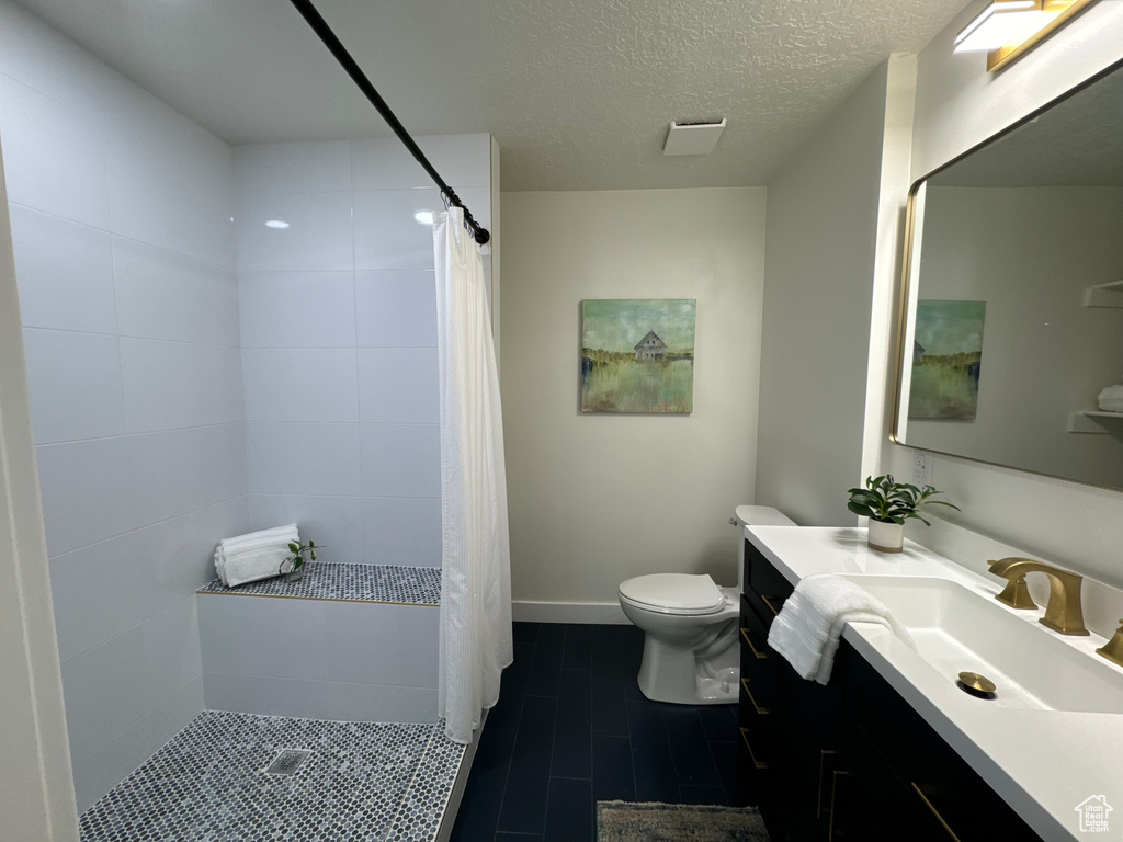 Full bath featuring vanity, a tile shower, a textured ceiling, and tile patterned flooring