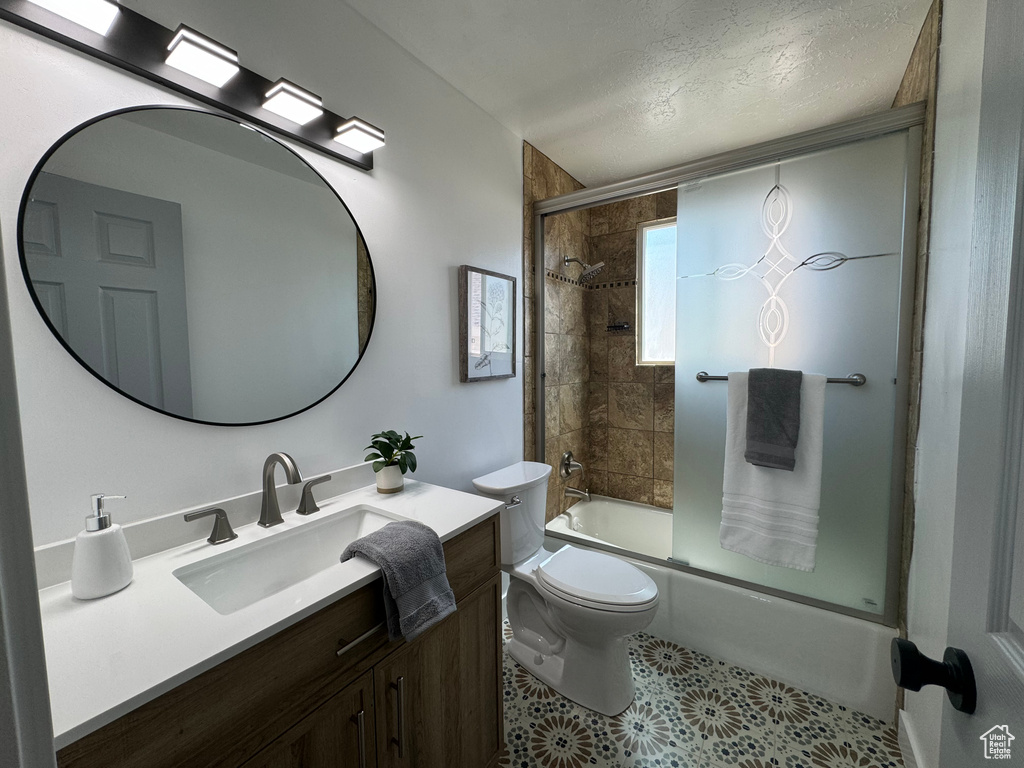 Bathroom with vanity, combined bath / shower with glass door, tile patterned floors, and a textured ceiling
