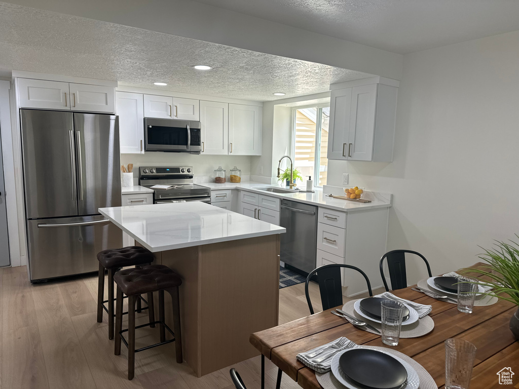 Kitchen with appliances with stainless steel finishes, a textured ceiling, light wood finished floors, a kitchen island, and white cabinetry