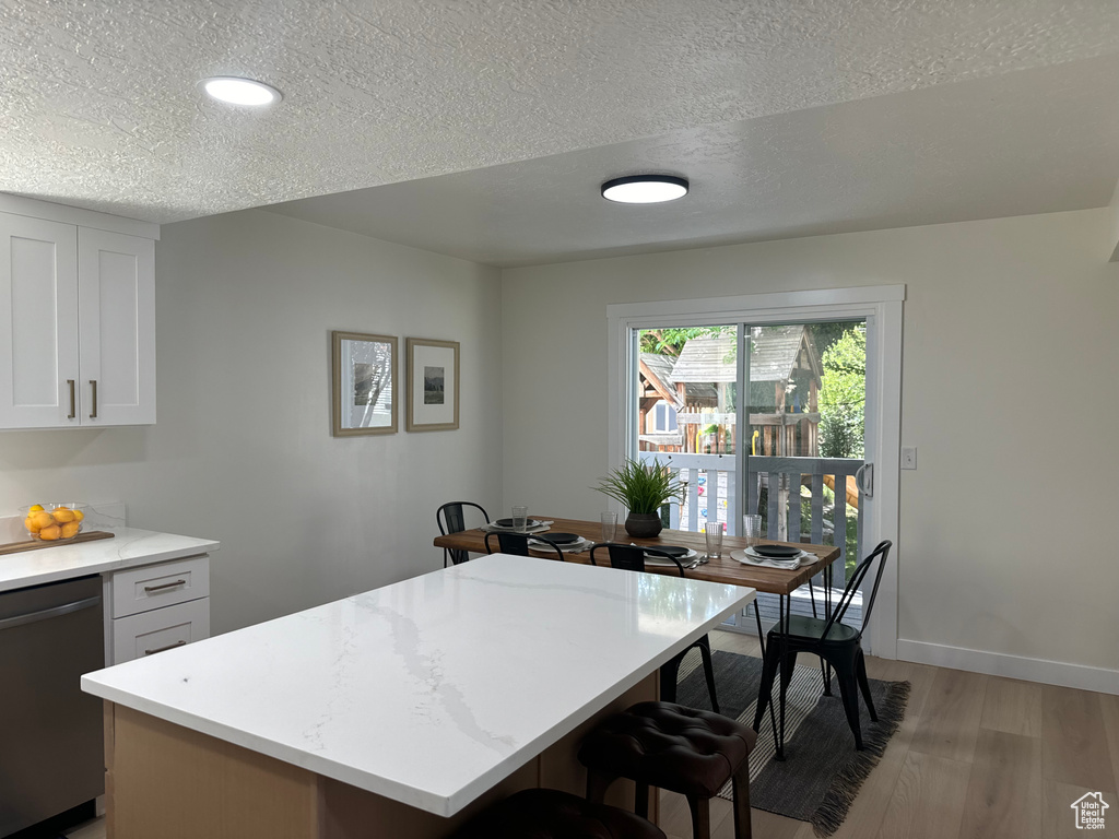 Kitchen with stainless steel dishwasher, light wood-style floors, a breakfast bar area, light countertops, and a textured ceiling