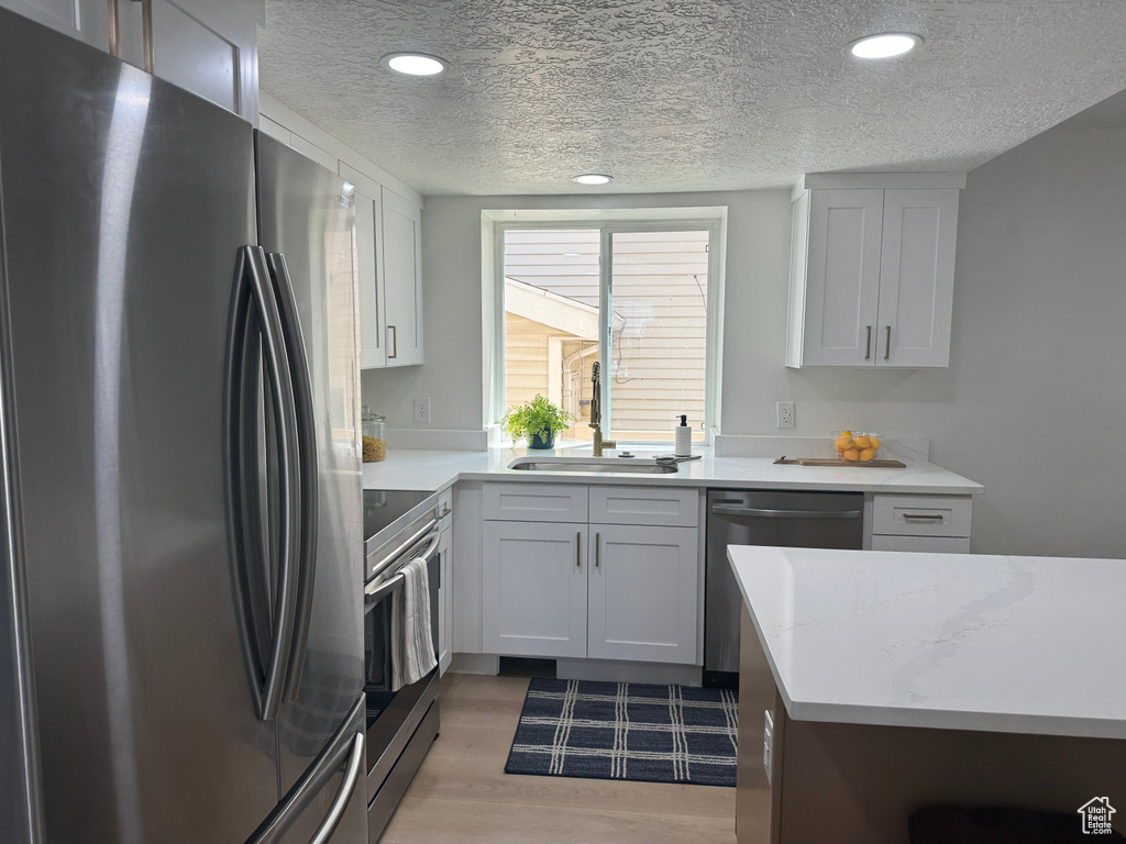 Kitchen with stainless steel appliances, a textured ceiling, light wood-style flooring, recessed lighting, and white cabinetry