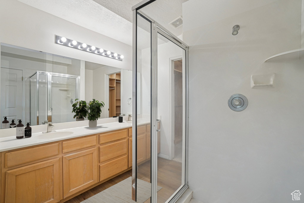 Bathroom with a shower stall, double vanity, a spacious closet, and wood finished floors