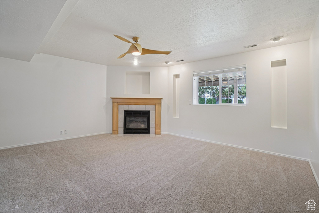 Unfurnished living room featuring ceiling fan, a tile fireplace, carpet floors, and a textured ceiling