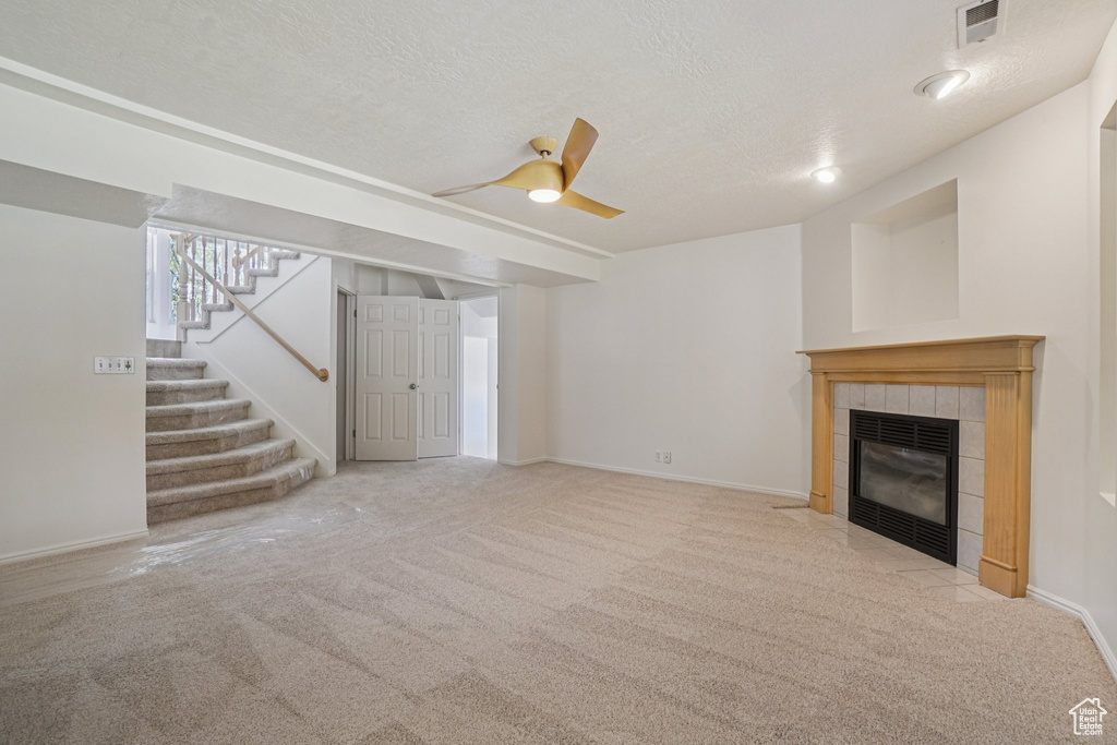 Unfurnished living room with a fireplace, carpet flooring, stairs, ceiling fan, and a textured ceiling