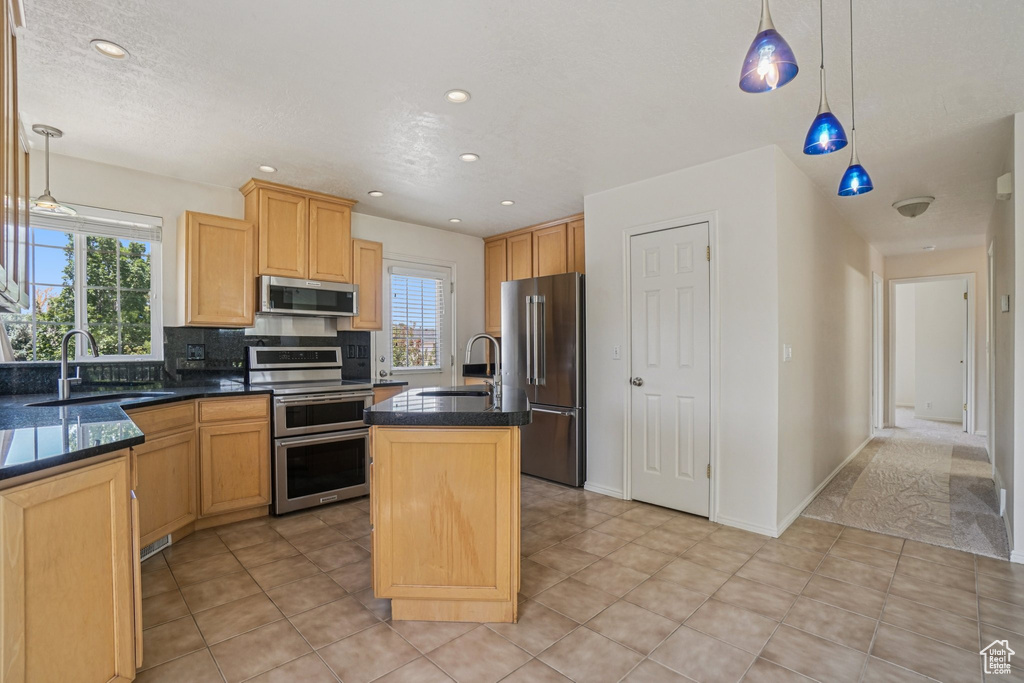 Kitchen featuring appliances with stainless steel finishes, a center island with sink, backsplash, hanging light fixtures, and recessed lighting