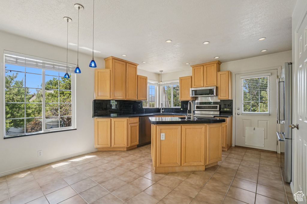 Kitchen featuring stainless steel appliances, dark countertops, backsplash, recessed lighting, and a center island with sink