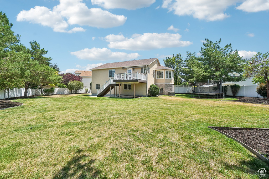 Rear view of house featuring stairs, a trampoline, a fenced backyard, a deck, and stucco siding