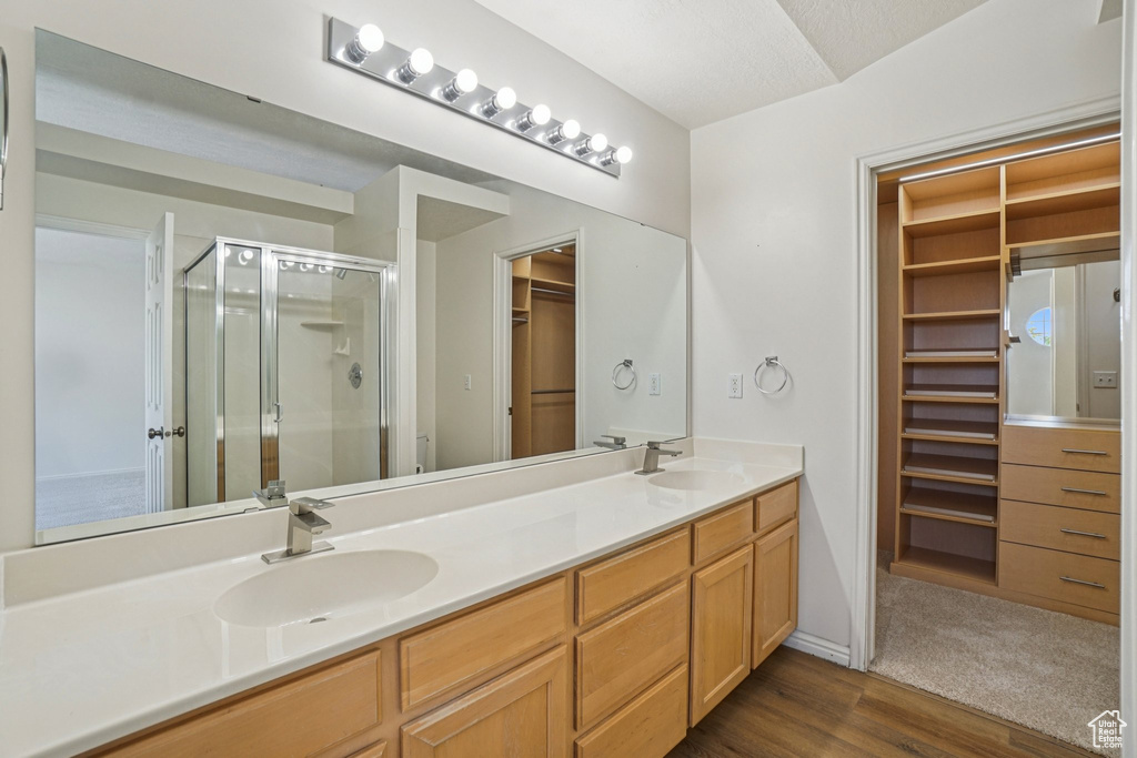 Bathroom with a shower stall, double vanity, a walk in closet, and wood finished floors