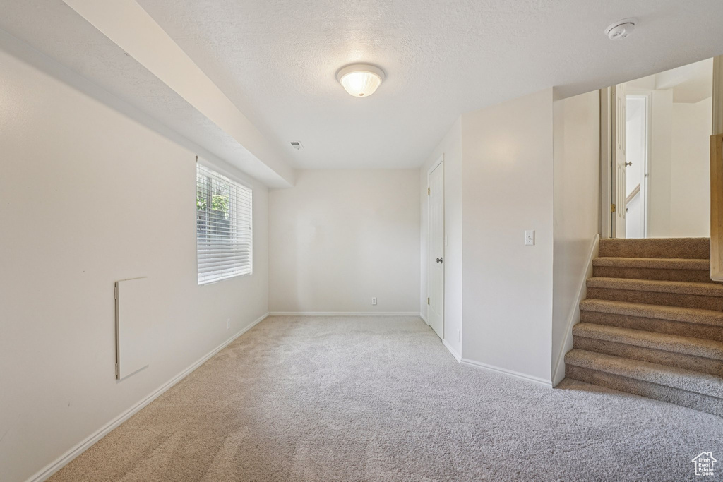 Carpeted spare room featuring a smoke detector, stairs, and a textured ceiling