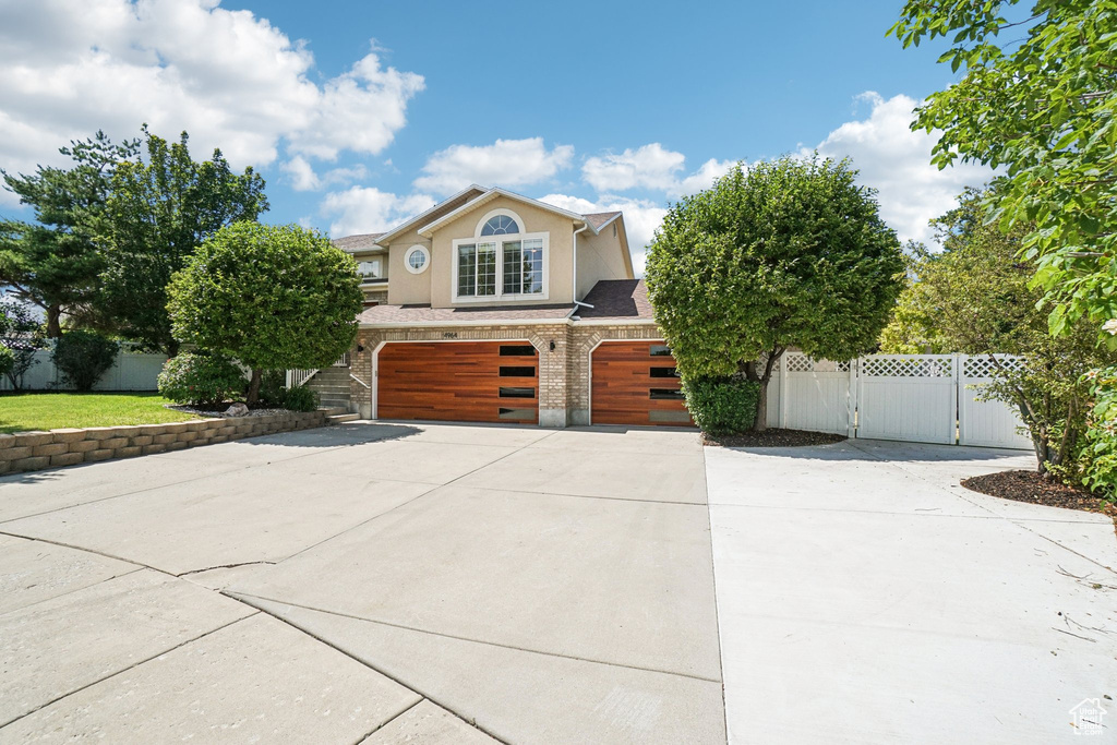 View of front of house with an attached garage, a gate, driveway, and stucco siding