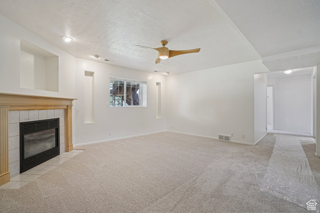Unfurnished living room with carpet floors, ceiling fan, a tiled fireplace, and a textured ceiling