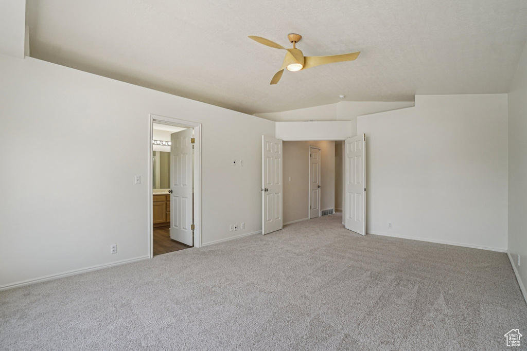 Unfurnished bedroom featuring carpet floors, lofted ceiling, connected bathroom, and ceiling fan