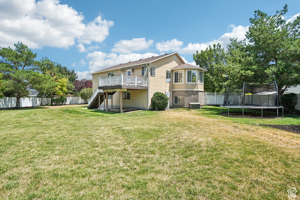 Back of property featuring stairway, a trampoline, a deck, and a fenced backyard