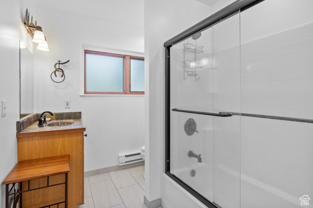 Full bathroom featuring a baseboard radiator, vanity, shower / bath combination with glass door, and tile patterned floors